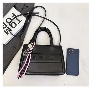 Close-up of black leather tote bag with brand embossing and tennis racket charm detail