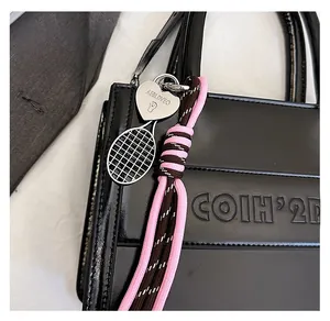 Detail of tennis racket charm and braided pink rope on black glossy leather tote