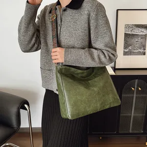 Grüne Retro-Tragetasche aus Leder mit breitem Ethno-Gurt an einem Modell gezeigt