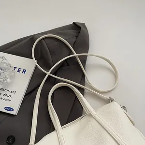 Macro detail of creamy white lychee grain leather handbag on a grey blazer