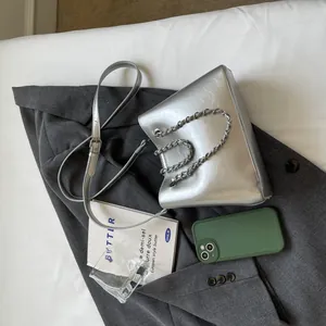 Close-up of metallic silver bucket bag with chain handle on grey blazer background