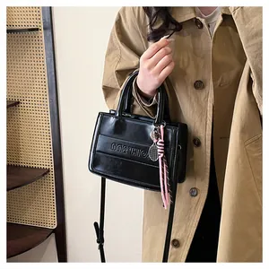 Detail of black faux leather tote featuring embossed letters and pink tassel charm