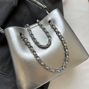 Close-up of metallic silver bucket bag with woven chain strap on dark fabric