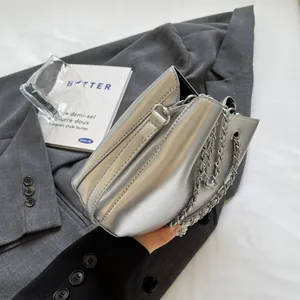 Close-up of metallic silver bucket bag with chunky chain strap on a grey suit