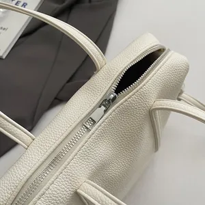 Close-up of beige lychee grain leather handbag with silver zipper and double handles