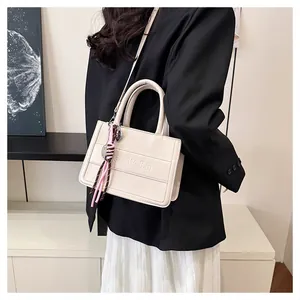 Detail view of cream vintage tote bag with embossed letters and woven accessory on a model
