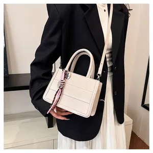 Close-up of beige faux leather tote with embossed logo and pink woven heart charm