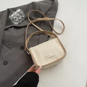 Details der vertikalen Plisseestruktur und des silbernen Logo-Schilds an der Handtasche