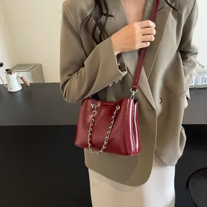 Detail of burgundy glossy leather bucket bag with silver metal chain and shoulder strap