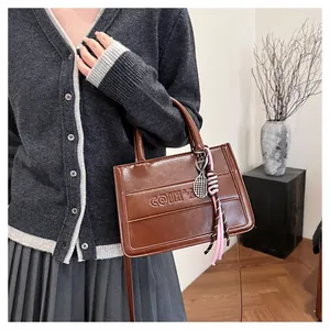 Close-up of brown faux leather tote with embossed logo and decorative metal tennis racket charm