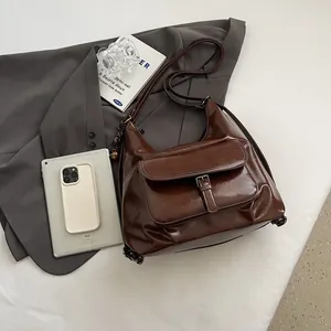 Deep brown oil wax leather crossbody bag shown with iPad and blazer for size reference
