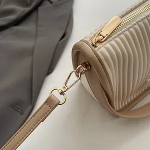 Makroansicht der beigen Faltenledertextur und goldfarbenen Metallbeschläge der Handtasche