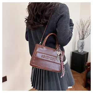 Close-up of vintage brown tote bag with leather texture, lettering and tennis pendant