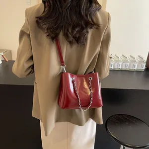 Detail of wine red bucket bag with glossy finish and chain, shown on model in a suit
