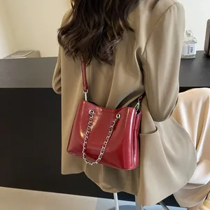 Detail view of burgundy patent leather bucket bag with elegant silver chain accent