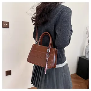 Brown leather tote bag detail with logo texture and pink braided charm on model