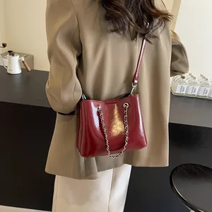 Detail of dark red glossy leather bucket bag with silver chain strap and refined finish