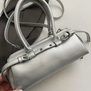 Detail of silver cylindrical handbag featuring metallic finish and decorative buckle straps