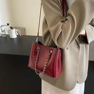 Close-up of wine red glossy patent leather bucket bag with silver chain handle and strap