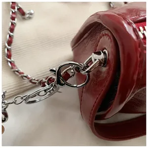 Close-up of silver lobster clasp and woven leather chain on dark red shoulder bag