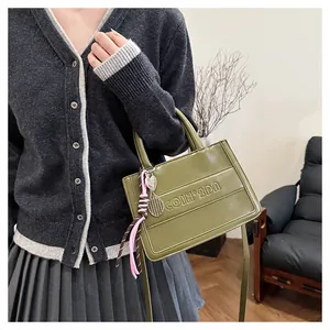 Close-up of avocado green faux leather tote with embossed text and tennis racket charm