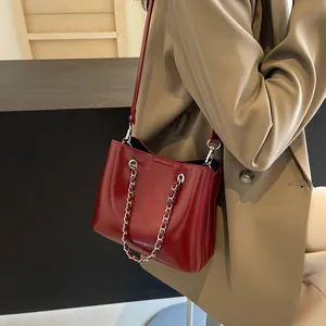 Detail of dark red glossy patent leather shoulder bag with silver chain strap handle