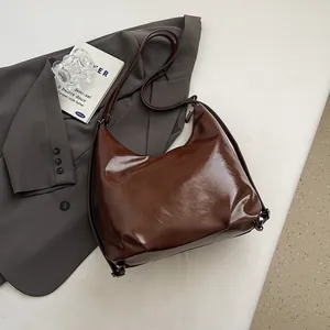 Close-up of a vintage dark brown oil wax leather shoulder bag on a grey blazer background
