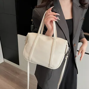 Detail of cream white litchi pattern leather handbag held by model in casual suit