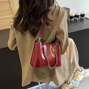 Close-up of a burgundy patent leather tote bag with silver chain on a model shoulder