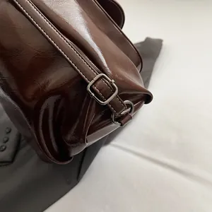 Detailed close-up of dark brown glossy leather bag with white stitching and silver buckles