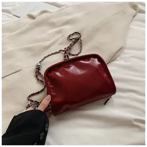 Detail of dark red glossy patent leather square bag with silver chain and ball buckle