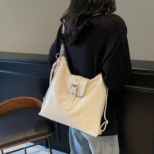 Detail view of large cream leather tote bag with buckle and adjustable strap on a model