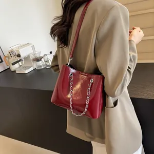 Detail of burgundy patent leather bucket bag with silver chain strap on model arm