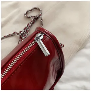Close-up of shiny red leather bag with silver metal zipper and chain strap detail