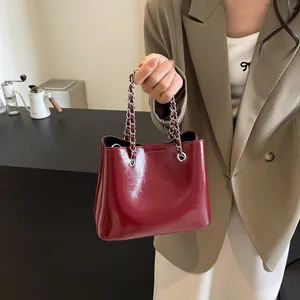 Detail view of burgundy patent leather bucket bag with silver metal chain handle