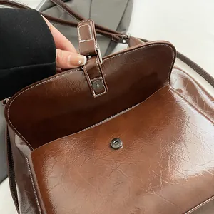 Close-up of brown glossy shoulder bag showing magnetic closure and white contrast stitching