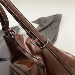 Detail of dark brown glossy leather bag with white contrast stitching and silver hardware
