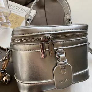 Detailaufnahme der silbernen Koffer-Handtasche mit Reißverschluss und Ledergriff