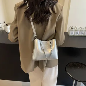 Silver metallic crossbody bag with chain detail shown on a model in a brown blazer