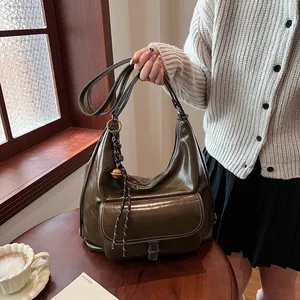 Detail of dark olive green hobo bag in glossy leather with decorative bell charm