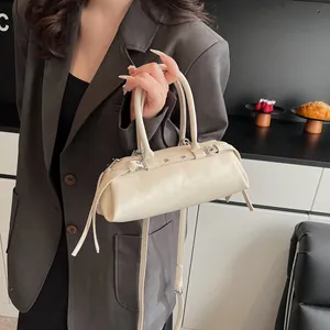 Detail of off-white baguette bag featuring long cylindrical handles and metal rivet accents