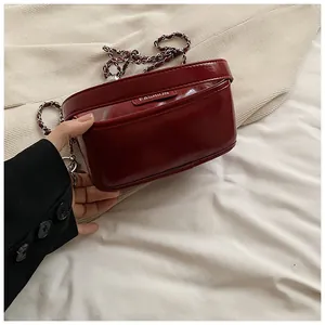 Detail of burgundy patent leather crossbody bag with chain strap and silver logo tag