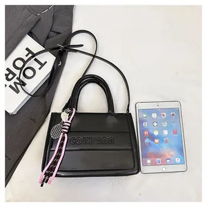 Close-up of black tote bag featuring embossed logo and a creative tennis racket charm