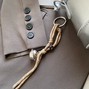 Detail eines Taschenanhängers mit khakifarbener Kordel, Saturn-Anhänger und Perle
