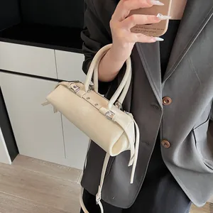 Detail of cream baguette bag featuring silver buckles, drawstring side and top handles