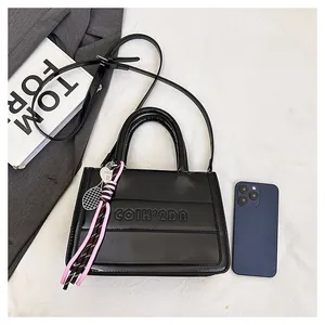 Detail of black glossy leather tote with embossed letters and a mini tennis racket charm