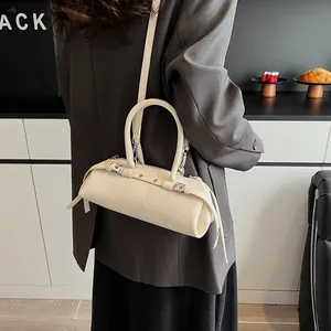 Detail view of cream barrel bag showing glossy leather texture and stylish rivet accents