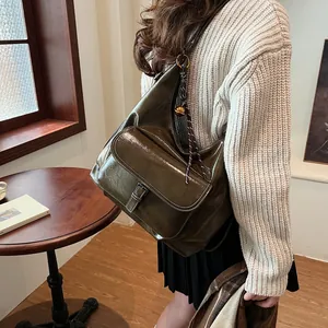 Detail of glossy olive green shoulder bag with metallic buckle and woven bell charm