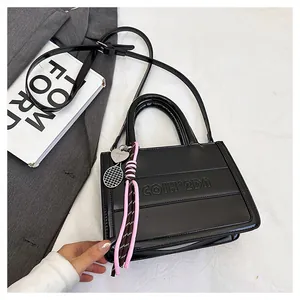 Detail of black patent leather tote bag featuring tassel charm and tennis racket pendant