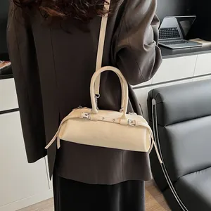 Detail of a creamy white baguette bag with silver grommet strap and polished finish